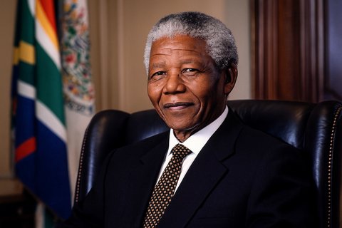 Нельсон Мандела в зрелом возрасте, в строгом костюме и галстуке, улыбается на официальном портретном фото